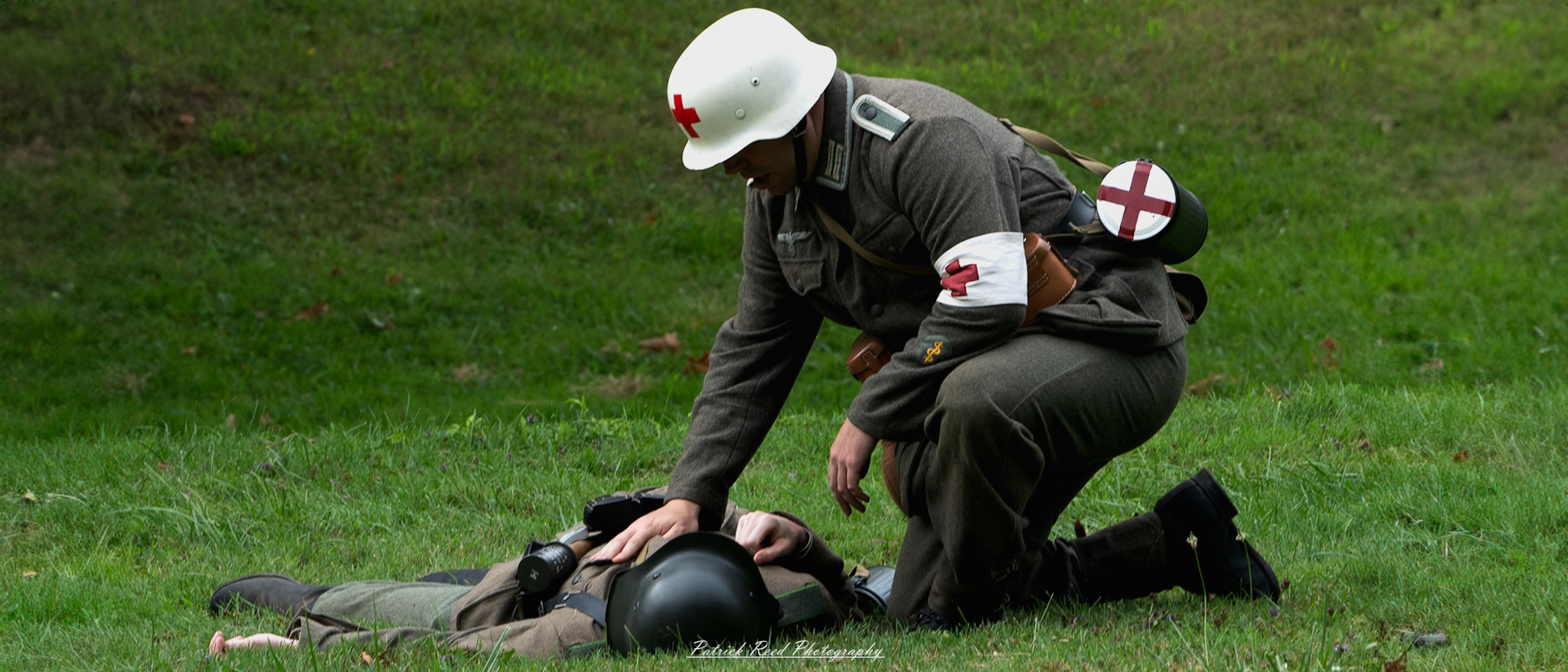 A poignant image of a German medic attending to a soldier lying on his back in a field. The medic is focused on providing care, illustrating the urgency and compassion of battlefield medicine during World War II in a moment of crisis.